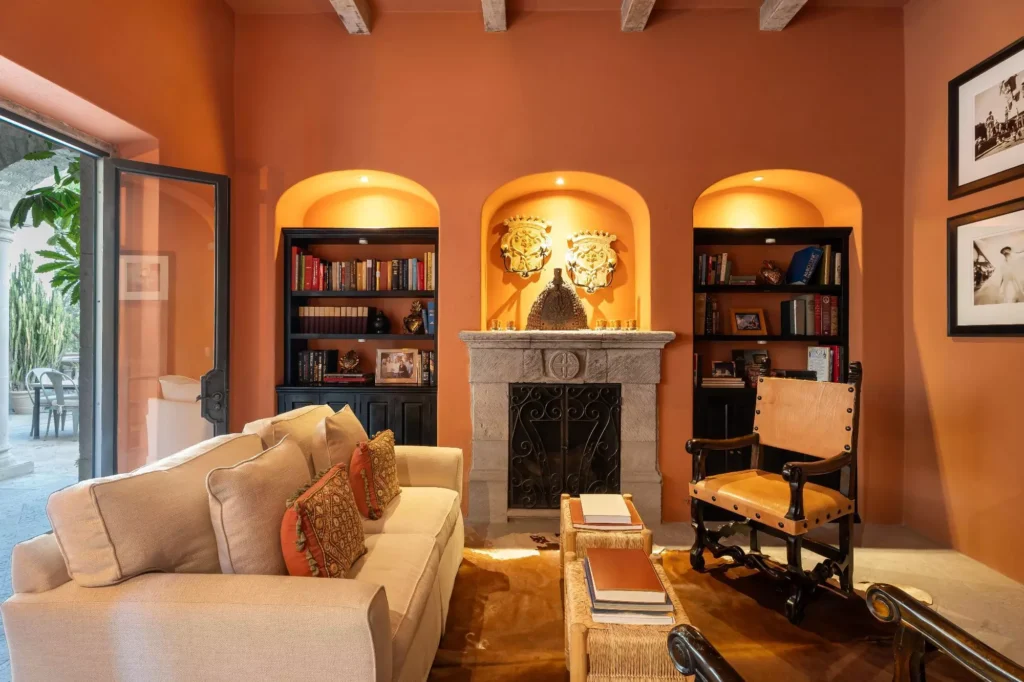 Biblioteca con muros en tono terracota, nichos empotrados y chimenea de cantera en propiedad de Guadiana, San Miguel de Allende